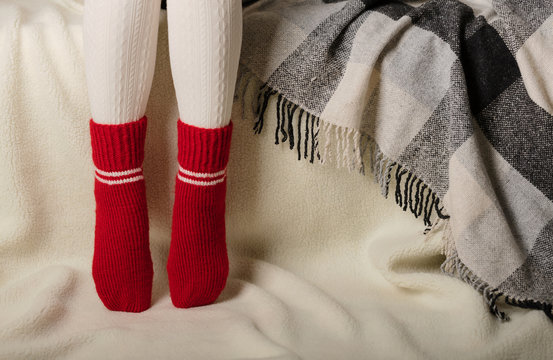 Female legs in warm white knitted tights and red socks on a white background made of faux fur