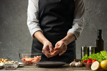 The chef processes shrimps for seafood salad at the home kitchen. Background from a concrete wall with a text area for restaurant menu design
