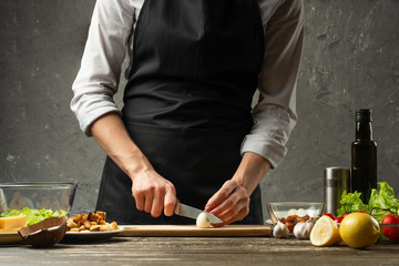 Chef cuts quail eggs for a vegetarian salad with seafood on the background of a concrete wall