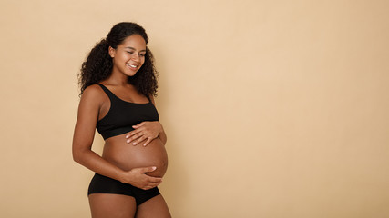 Side view of happy pregnant woman holding her belly