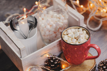 hot cocoa with marshmallows on wooden table with christmas lights. Cozy winter home concept