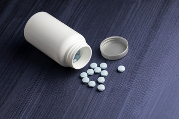Medication bottle and blue pills spilled over blue wood background. Pharmaceutical drugs.