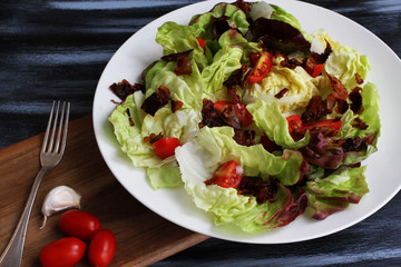 Red lettuce salat in white plate on dark board with cherry tomatoes, bacon and cheese