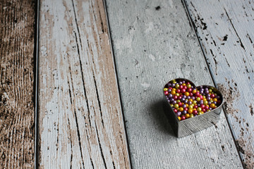 Heart cookie cutters with colorful sugar balls on wooden board, high angle view, close-up, copy...