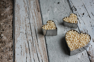 Heart cookie cutters with pearly sugar balls on wooden board, high angle view, close-up, copy space