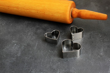 Heart cookie cutters with golden and silver sugar balls, wooden trowel on dark board
