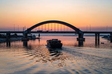 Fishing boat through the bridge, sunset background