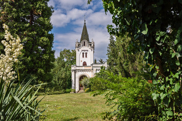 Fototapeta na wymiar chapel with bell tower among the trees in the park and blue sky