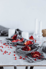 chunks of ripe red pomegranate, fork and knife on a grey kitchen towel on a grey white background with candles, seeds