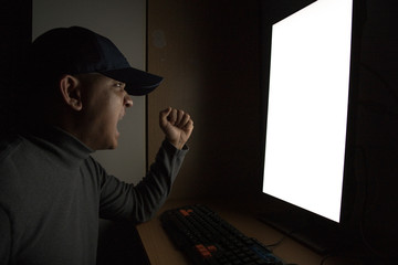 Side view of man Hacker sit at the computer monitor and angry and upset feeling in the dark room.