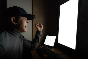Side view of man Hacker sit at the computer monitor, White screen tablet and angry and upset feeling in the dark room.