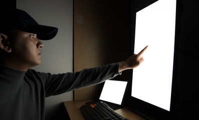 Side view of man Hacker sit at the computer monitor, white screen tablet pointing fingers monitor in the dark room.