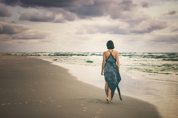 young woman in a sexy long dress walking along the beach at sunrise or sunset