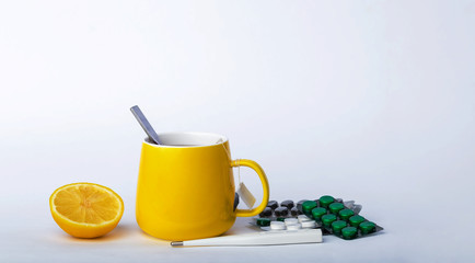 A yellow cup of tea with lemon, a thermometer and pills for treatment Cold And Flu. Prevention of colds and flu on grey background