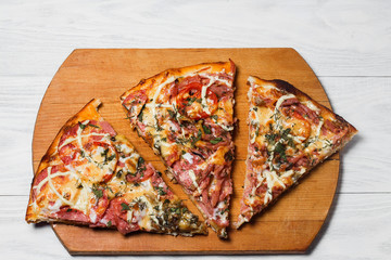 Italian rustic pizza, three pieces on a wooden tray, white wooden table, with tomatoes and cheese