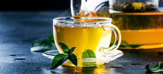 Hot chinese green tea with mint, with splash pouring from the kettle into the cup, steam rises,...