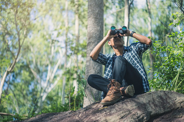 Man Hand Holding / looking / watching using Binoculars. A man looking through the binoculars. Young man is sitting on cliff's edge and looking to misty valley bellow.
