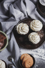 chocolate cupcakes with white cream s brown ceramic plate of ginger biscuits and chocolate spoons on the table with a kitchen towel food photo close-up