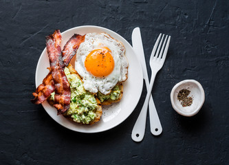 Healthy nutritious breakfast - avocado toast, bacon and fried egg on dark background, top view