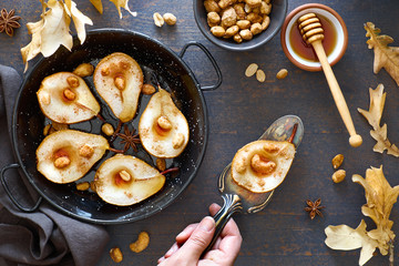 Flat lay with a tray of baked pears with caramelized nuts on dark wooden background with Autumn leaves