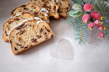 Christmas stollen on light stone board with fir twigs and berries.