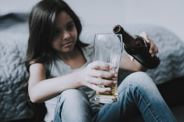 Little Girl Sits near Bed and Pours Beer in Glass
