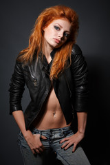 Portrait of young sexy redhead girl in leather jacket on dark background in studio