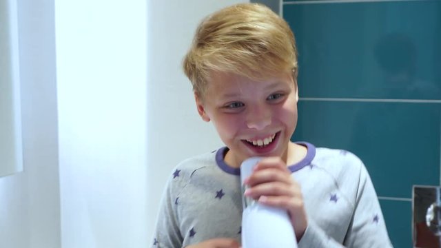 Front view of happy cute little boy sings song in bathroom using hair dryer as microphone. Portrait of happy creative future little singer. Real time 4k video footage.