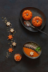 Traditional pumpkin homemade cream-soup with seeds, crackers and little pumpkins. Close up, top view on the dark wooden background