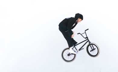 Fototapeta na wymiar Young man in casual clothing makes tricks on bmx against the background of a white wall. BMX rider makes the Barzpin trick against its white background