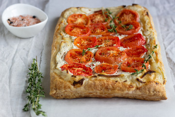 Deliciously simple tomato tart, puff pastry topped with cream cheese or ricotta and tomatoes on parchment paper. Summer tart. Top view. Copy space