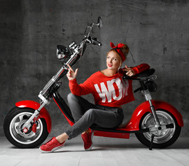 Obraz na płótnie Canvas Woman sitting on motorcycle bicycle scooter retro pinup style pointing finger at the corner in red blouse and jeans