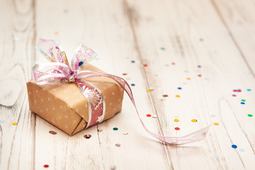 brown gift box with ribbon  on white wooden board background with confetti. Selective focus