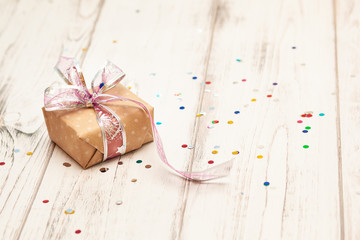 brown gift box with ribbon  on white wooden board background with confetti. Selective focus