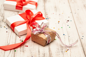 Gift boxex with thin red ribbon and confetti on old white wood table. Selective focus