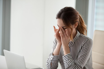 Tired young woman massaging nose bridge at workplace. Businesswoman experiences discomfort from long work at computer. Bad eye vision concept