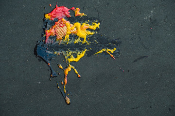 fallen red and yellow ice cream on gray asphalt.