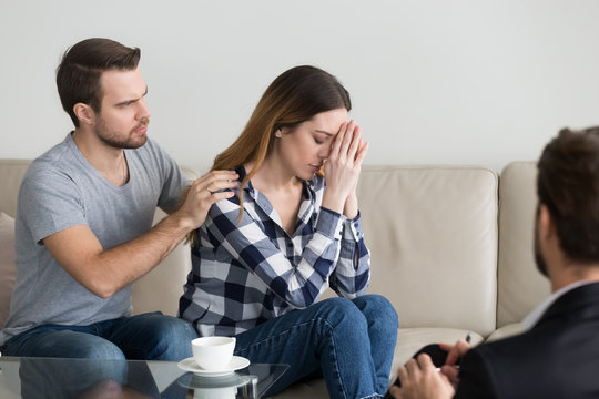 Young man, husband calming, supporting, consoling hopeless woman. Desperate, sad sensitive woman covering her face with hands listening to doctor. Family problems, distrust, attempt to save marriage