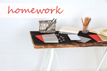 Desk with school supplies and word HOMEWORK on brick wall background