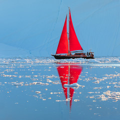 Beautiful red sailboat in the arctic next to a massive iceberg showing the scale. Ilulissat, Disko Bay, Greenland. © Kertu