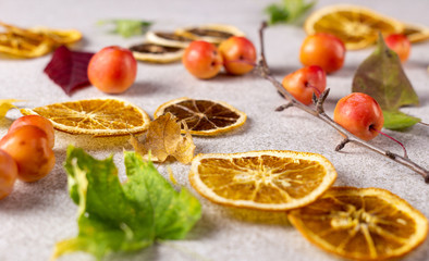 Dried sliced lemons and oranges with fresh red apples and autumn leaves on white texture surface.