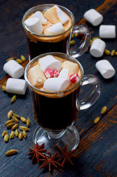 Hot chocolate in the glasses with marshmallows decorated with winter spices - cinnamon, cardamom and anise on the black wooden background. Side view