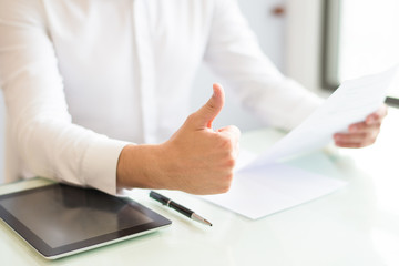 Closeup of man holding document and showing thumb up. Entrepreneur sitting at desk and working....