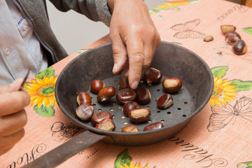 horizontal image with detail of two hands preparing chestnuts, inside a pan.