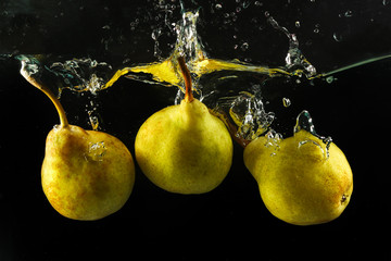 Fototapeta na wymiar Three pears splashing in water on black