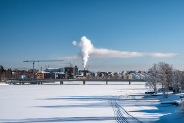 View of factory power plant at middle of city in winter with steam rising into deep blue sky