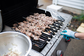 Barbecue on a grill, person with a glove rotating one of skewers.