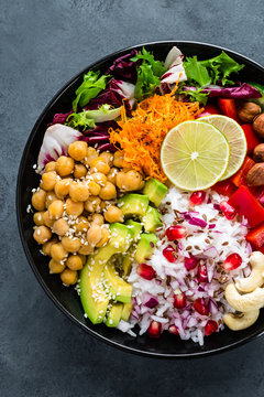 Healthy vegetarian Buddha bowl with fresh vegetable salad, rice, chickpea, avocado, sweet pepper, cucumber, carrot, pomegranate and nuts closeup