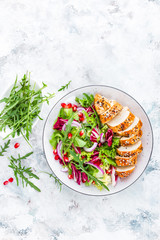 Grilled chicken breast, fillet and fresh vegetable leafy salad with arugula and pomegranate on plate