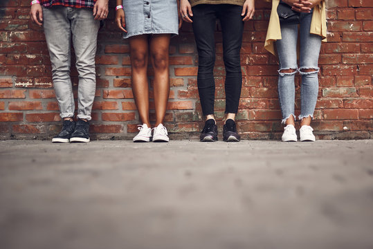 Legs of friends. Horizontal image of four stylish people standing next to the brick wall and posing for the photo
